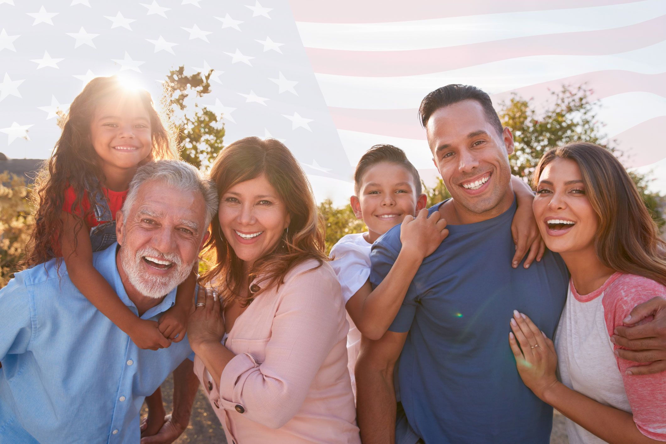 Familia hispana sonriendo al aire libre frente a una bandera de EE. UU.